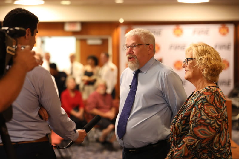 A reporter talks to Mike Button (center) at an appreciation ceremony where Stephanie Button (right) was presented with the